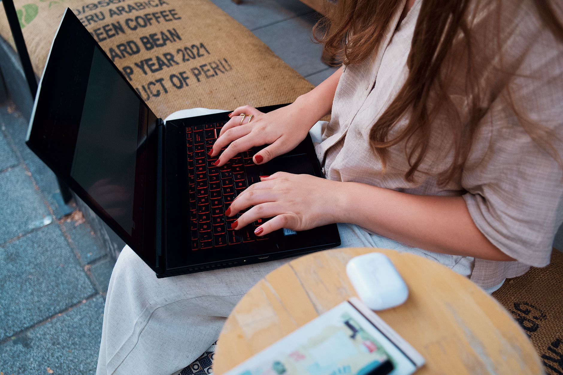 Žena s dlouhými vlasy pracuje na notebooku v kavárně, soustředí se na práci na dálku.